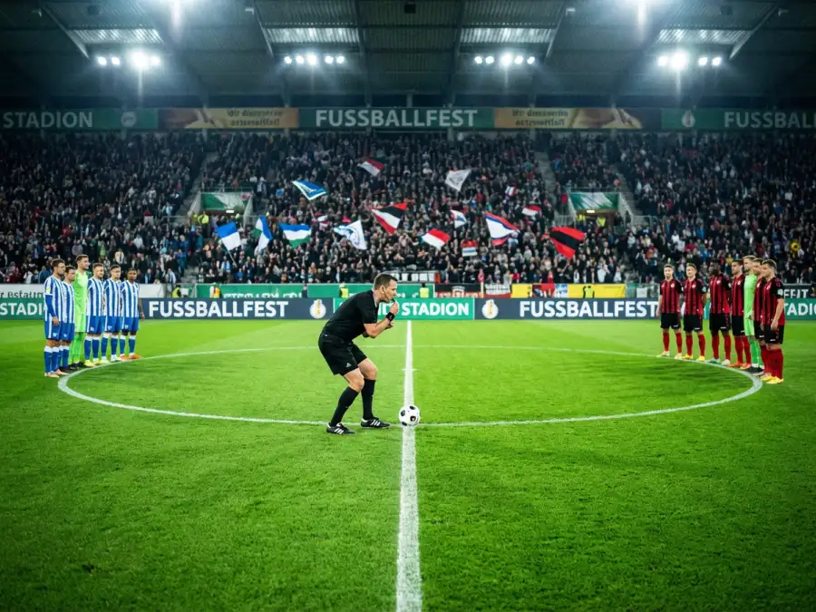 Fußballfeld mit Spielern aus verschiedenen Nationen beim Anstoß einer WM-Gruppenpartie unter Flutlicht