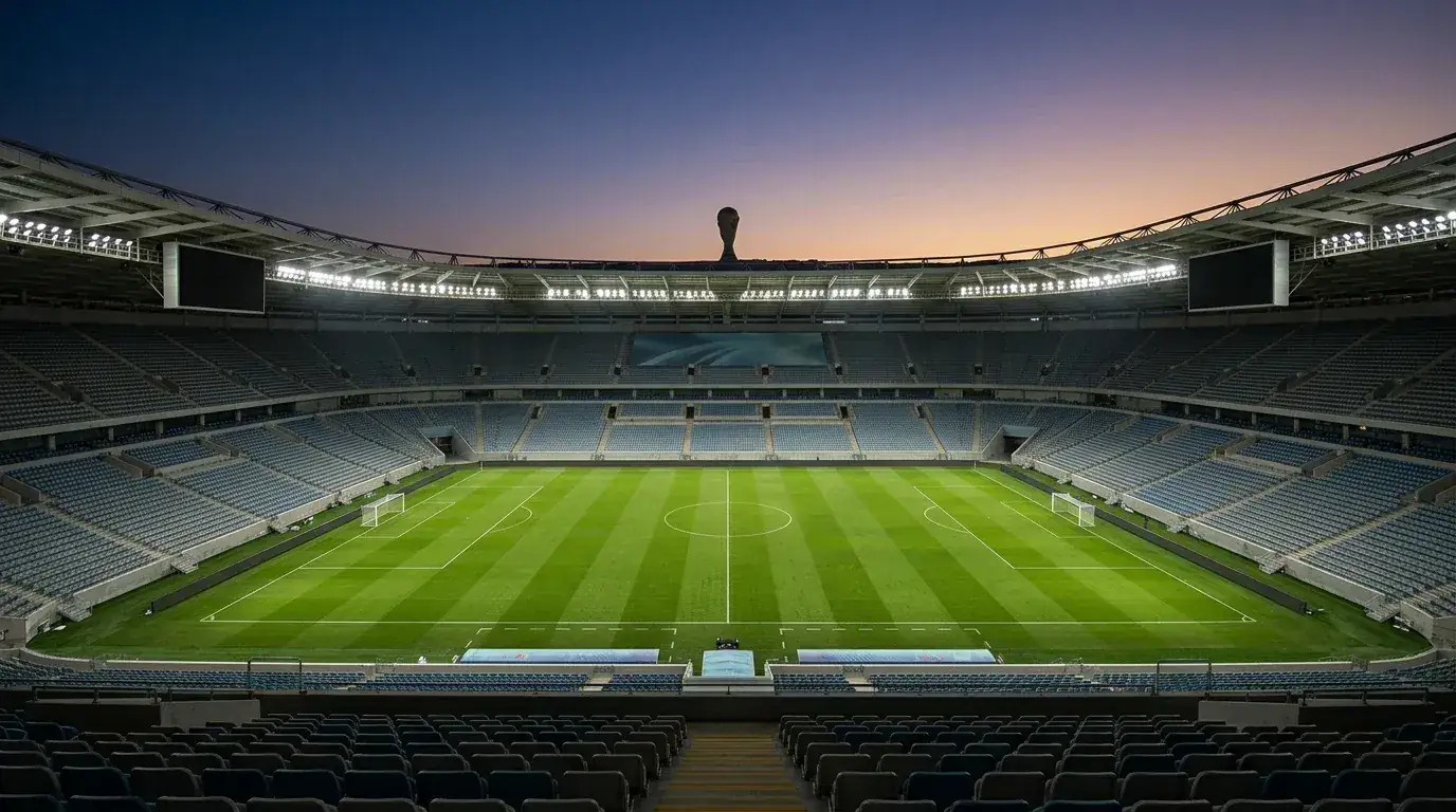 Leeres, flutlichtbeleuchtetes Fußballstadion in der Abenddämmerung vor einem großen Spiel, WM-Pokal-Silhouette am Horizont
